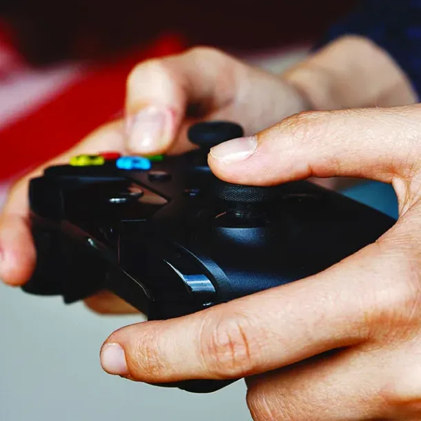 Close-up tangan memegang game controller; ilustrasi kebiasaan gaming remaja