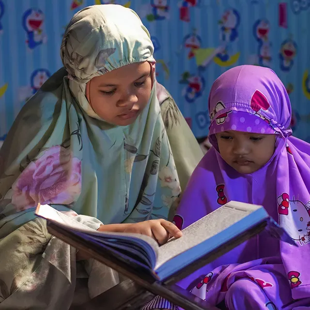 Kakak dan adik belajar membaca Al-Qur'an bersama di rumah